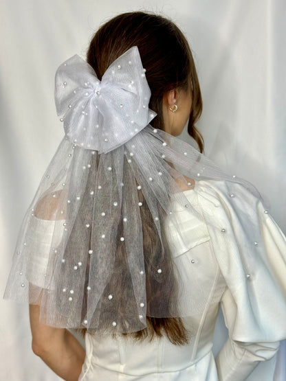 A bride wearing a white bridal gown and a double white tulle hair bow with beaded pearls, designed for special occasions.