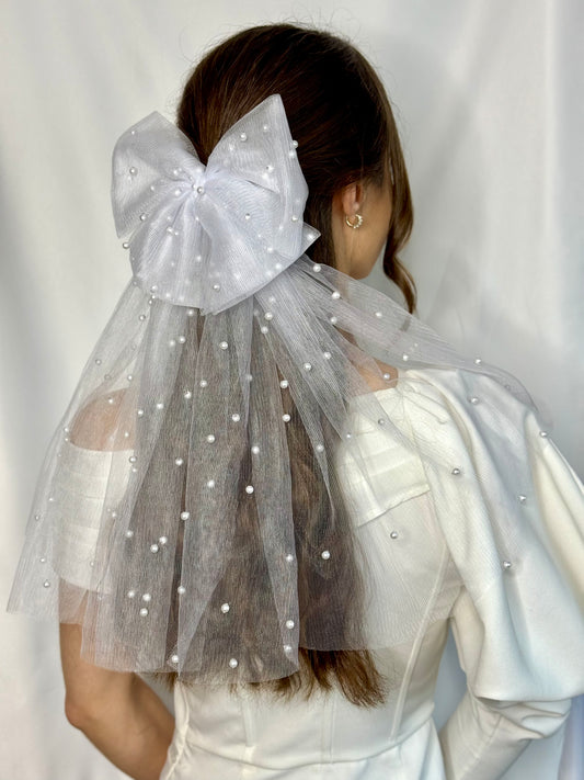 A bride wearing a white bridal gown and a double white tulle hair bow with beaded pearls, designed for special occasions.